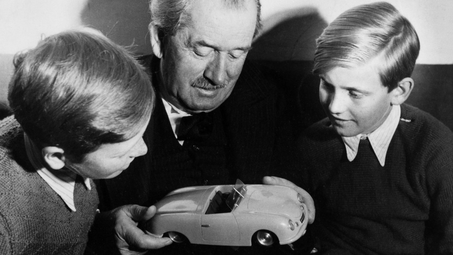FERDINAND PORSCHE EN 1949 MOSTRANDO A SUS NIETOS FERDINAND PIËCH (IZQUIERDA), Y AL HIJO DE FERRY, FERDINAND ALEXANDER (DERECHA), EL PORSCHE “BUTZI” UNA MAQUETA DEL PORSCHE 356/1
